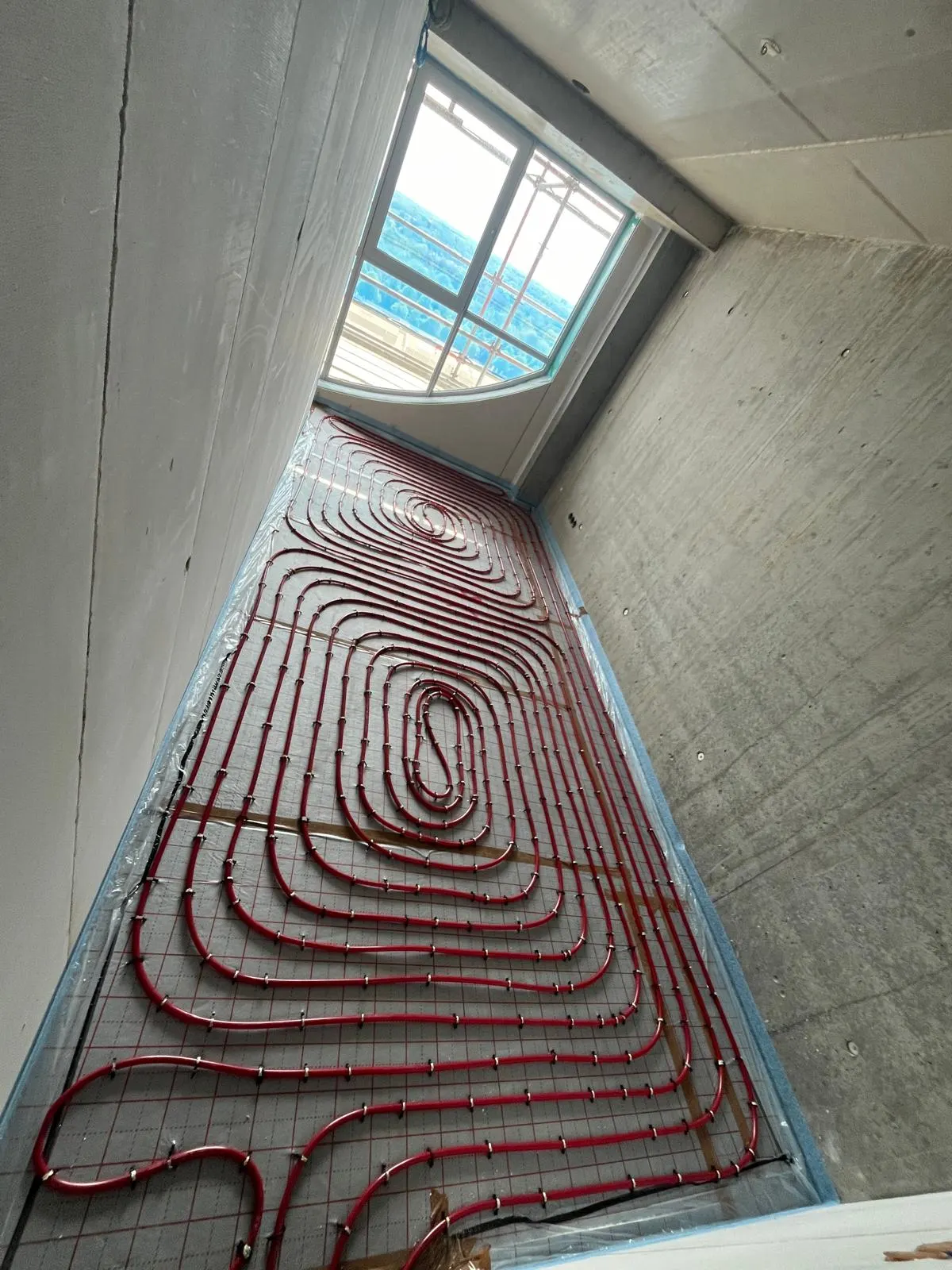 Buis in ruime lussen op een wapeningsnet in een appartement in ruwbouw, tussen een betonnen wand en een kalkzandsteenwand, met een pui op de achtergrond