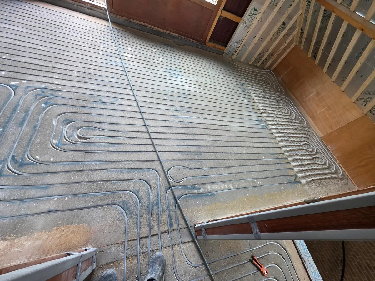 Vloerverwarmingsbuis in gefreesde groeven in droogbouwplaten op een zoldervloer, met een houten kapconstructie en isolatieplaten erachter