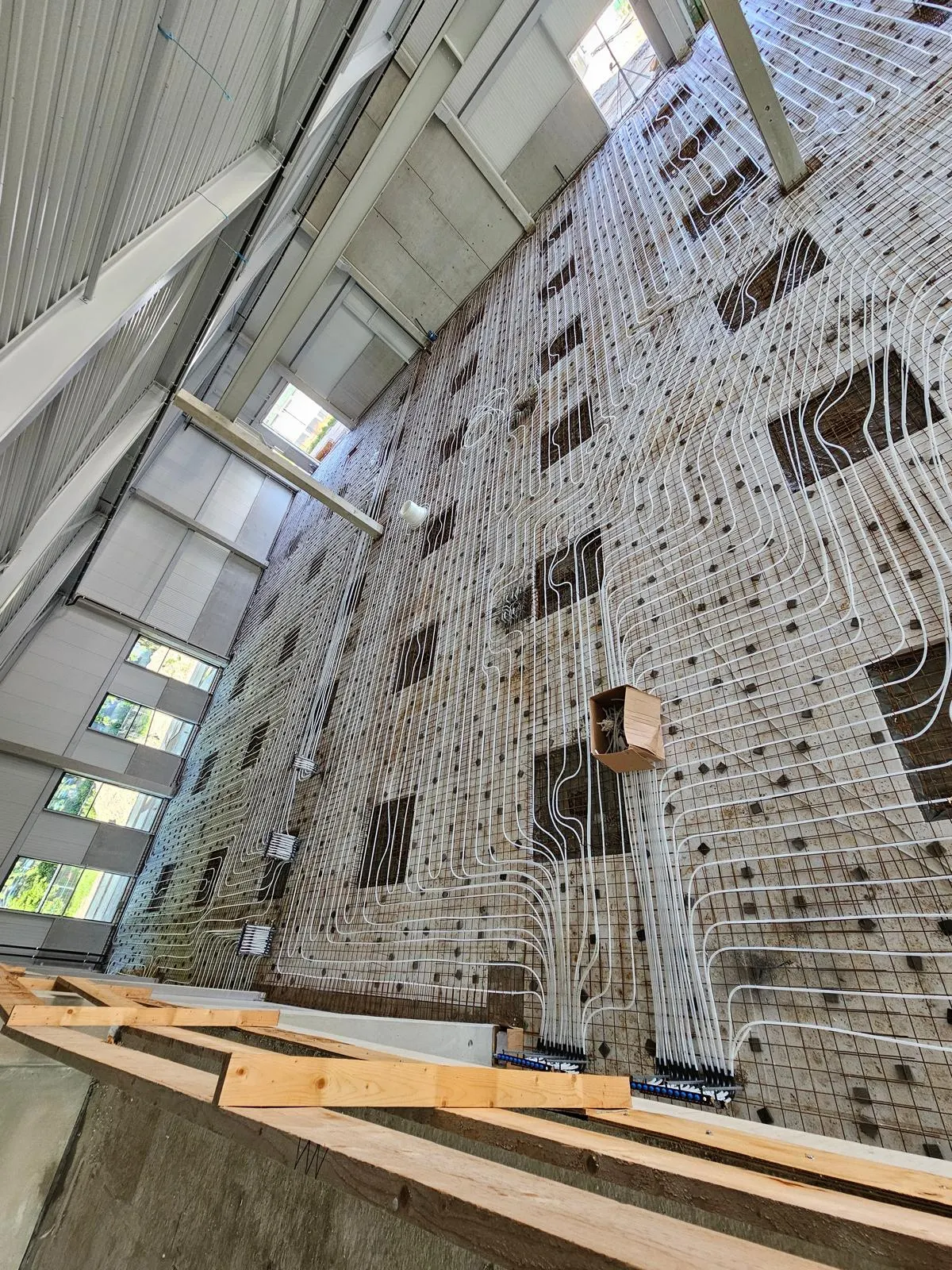 Vloerverwarmingsbuis in lange lussen op een wapeningsnet over de volle breedte van een bedrijfshal, met daglicht uit een rij hoge ramen