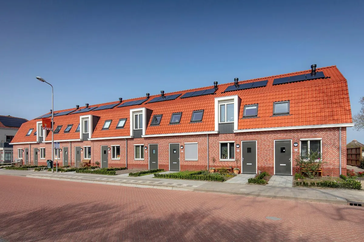 Een rij opgeleverde eengezinswoningen met rode pannendaken, dakkapellen en zonnepanelen, gezien vanaf de straat onder een blauwe lucht