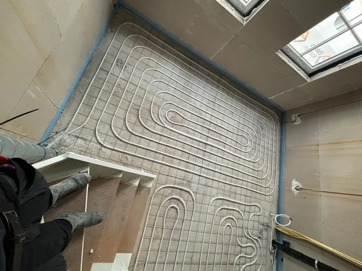 Buis in rechthoekige lussen op een wapeningsnet op een verdiepingsvloer, met een dakraam rechts, een trapgat met witte stootborden links en gele elektrabuizen langs de wand