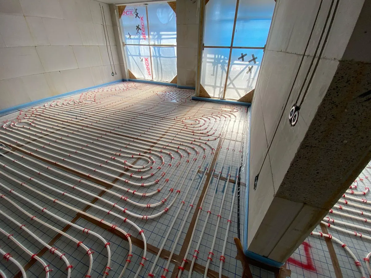 Buis in dichte lussen op een wapeningsnet langs een raamopening met een stenen vensterbank, met de elektraleidingen langs de wand