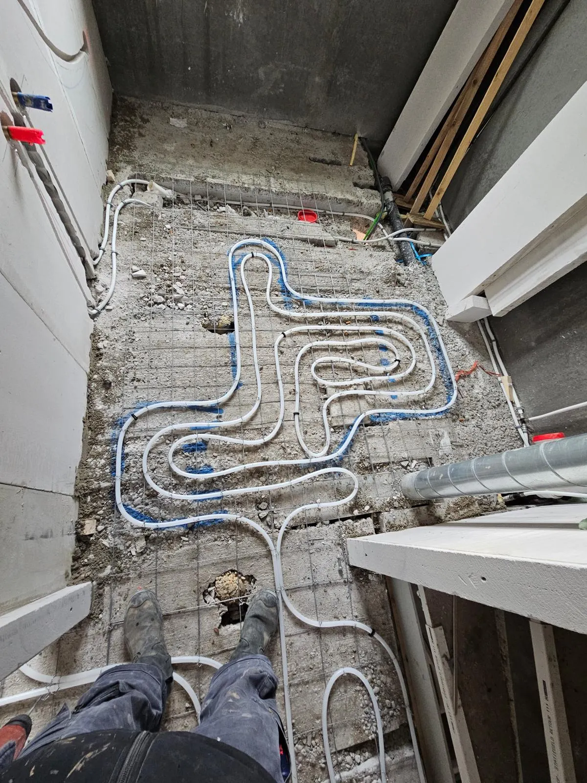 Vloerverwarmingsbuis in een korte lus op een wapeningsnet, op een gestripte betonvloer met blauwe uitzetmarkeringen