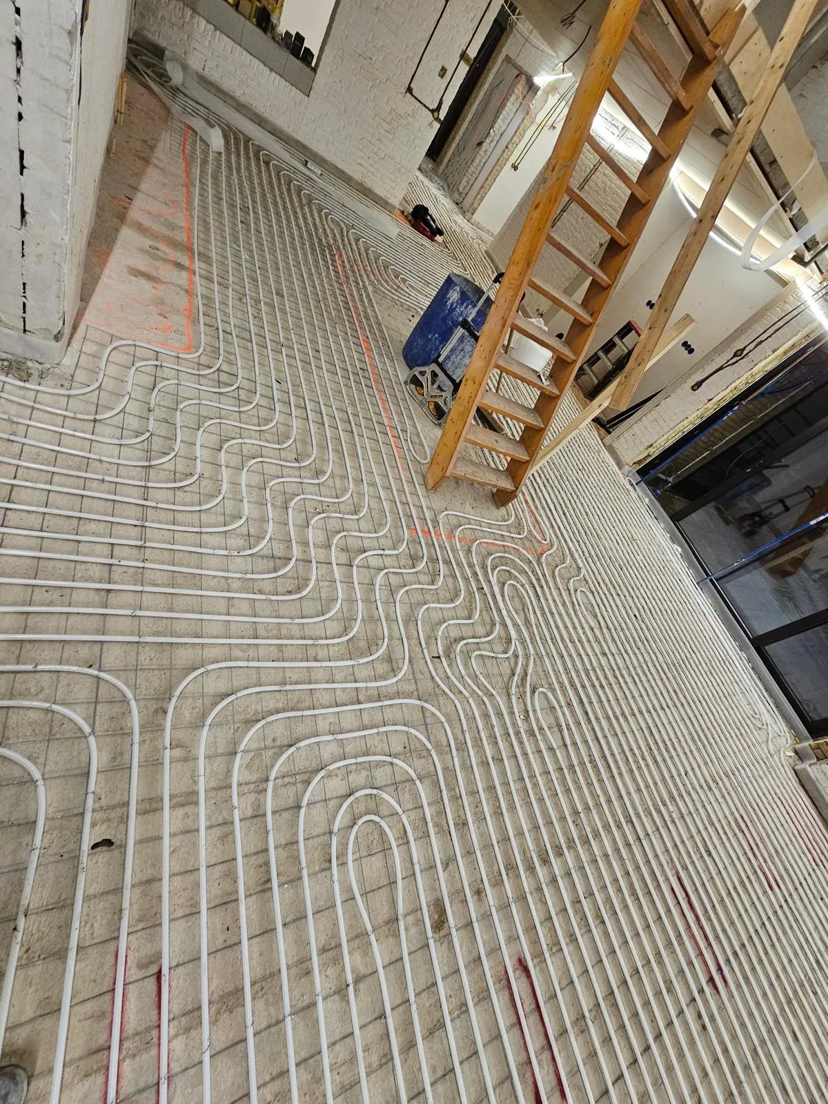 Buis in ruime lussen op een wapeningsnet in een hoge ruimte met witgeschilderde bakstenen wanden, met een houten trap ernaast en een pui op de achtergrond