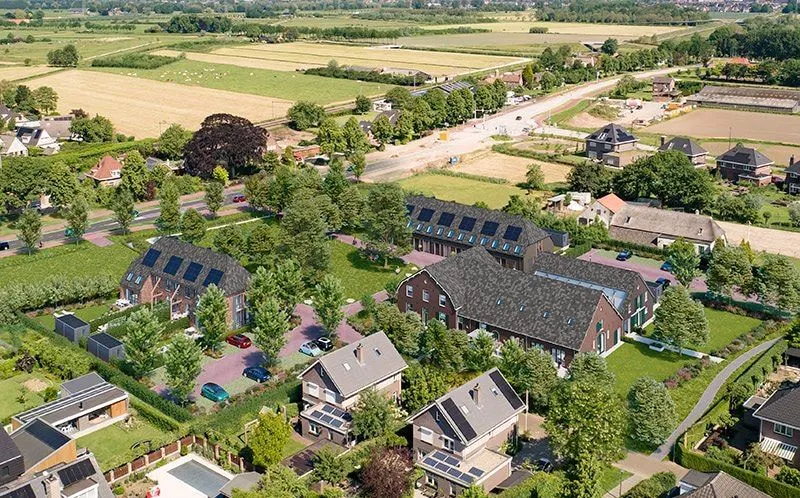 De nieuwbouw bij Wijchen, woningen met kappen en zonnepanelen tussen de weilanden, met de oudere schuren ernaast